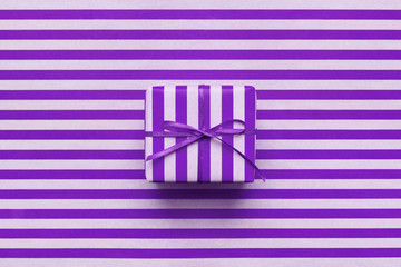 Wall Mural - Purple gift box on violet striped wrapping paper. Minimal design, geometric background for greeting card. Wrapping day concept.