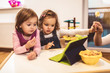 © Mediteraneo - Two adorable little sisters playing with a digital tablet at home.