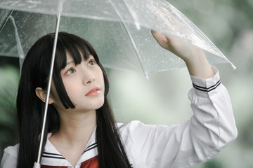 portrait of asian school girl walking with umbrella at nature walkway on raining