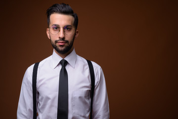 Wall Mural - Young handsome bearded Iranian businessman against brown backgro