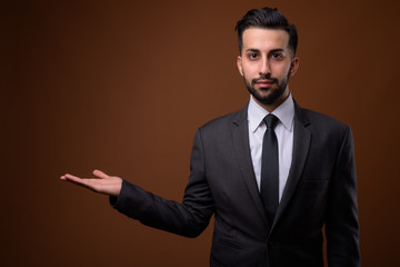 Young handsome bearded Iranian businessman against brown backgro