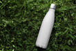 © Lalandrew - Stainless thermos water bottle isolated on green grass outdoor. White matte color. Horizontal photo without effects.