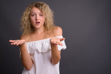 Young beautiful woman with blond curly hair against gray backgro