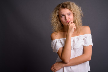 Young beautiful woman with blond curly hair against gray backgro