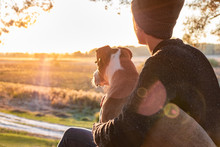 Hugging A Dog In Beautiful Nature At Sunset. Woman Facing Evening Sun Sits With Her Pet Next To Her And Enjoys Beauty Of Nature