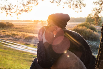 Wall Mural - Hugging a dog in beautiful nature at sunset. Woman facing evening sun sits with her pet next to her and enjoys beauty of nature