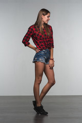 Wall Mural - Young beautiful woman teenager in a red checked shirt and torn denim shorts