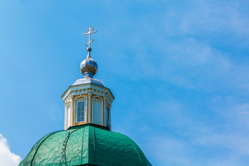 Green dome of a Christian temple with a silver cross against the blue sky with white clouds.