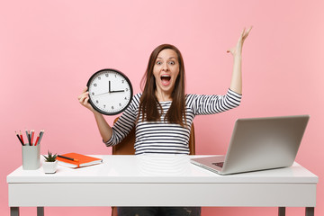 Wall Mural - Shocked woman screaming spreading hands holding alarm clock sit, work at office with pc laptop isolated on pastel pink background. Achievement business career concept. Copy space. Time is running out.