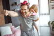 I am superman. Portrait of happy father is carrying his daughter on back and laughing. He is stretching hand forward. Man has make-up on face and hair curlers 