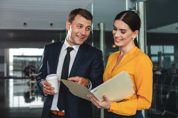 That is easy. Waist up portrait of happy man holding cup and looking at his female colleague with smile