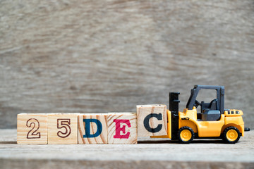 Toy forklift hold block c to complete word 25dec on wood background (Concept for calendar date 25 in month December)