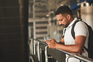 Pleasant serious Hindu man using his phone while standing at the railway station