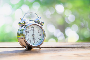 Vintage alarm clock on wooden table with green nature bokeh background.with copy space for text.