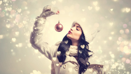 Wall Mural - Woman holding Christmas bauble on shiny hearts background