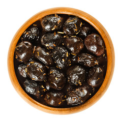 Wall Mural - French black olives with herbs in wooden bowl. Dried olives, olea europaea, preserved with olive oil, seasoned with Herbes de Provence. Isolated macro food photo closeup from above on white background