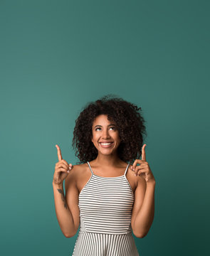 Smiling woman pointing fingers up over blue background
