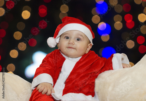 Cute Baby Wearing Santa Claus Costume On A Couch At Home In