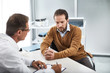 © Yakobchuk Olena - Adult doctor speaking with bearded man in his office while recording necessary data on paper
