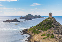 View Of Pointe De La Parata On The West Coast Of Corsica. A Ruined Genoese Tower Sits On Top Of The Rocky Promontory Overlooking The Archipelago Of The Sanguinaires And A Sailing Boat On A Sunny Day.