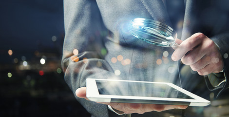 Wall Mural - Businessman examines a tablet with a magnifying glass. Concept of internet security