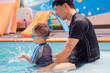 Cute little Asian 2 years old toddler boy child in swimming costume learn to swim at indoor salt water pool with father, Dad and son in Swimming school for small children, fun pool swim splash concept