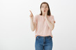 © Cookie Studio - Studio shot of surprised emotive attractive european woman in pink t-shirt, saying wow, folding lips and pointing up with index finger, expressing wonder and amazement, seeing something unbelievable