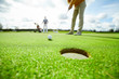 © pressmaster - One of golf players going to hit it right into the hole in lawn during game
