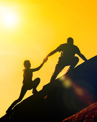 The joint work teamwork of two people man and girl travelers help each other on top of a mountain climbing team, a beautiful sunset landscape. The silhouettes on top of a mountain