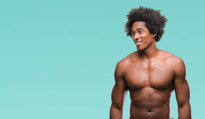 Wall Mural - Afro american shirtless man showing nude body over isolated background looking away to side with smile on face, natural expression. Laughing confident.