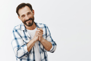 Wall Mural - Father being pleased of cute and touching drawing of child, tilting head and smiling, holding palms together while standing over gray background in casual shirt and grinning from having great family