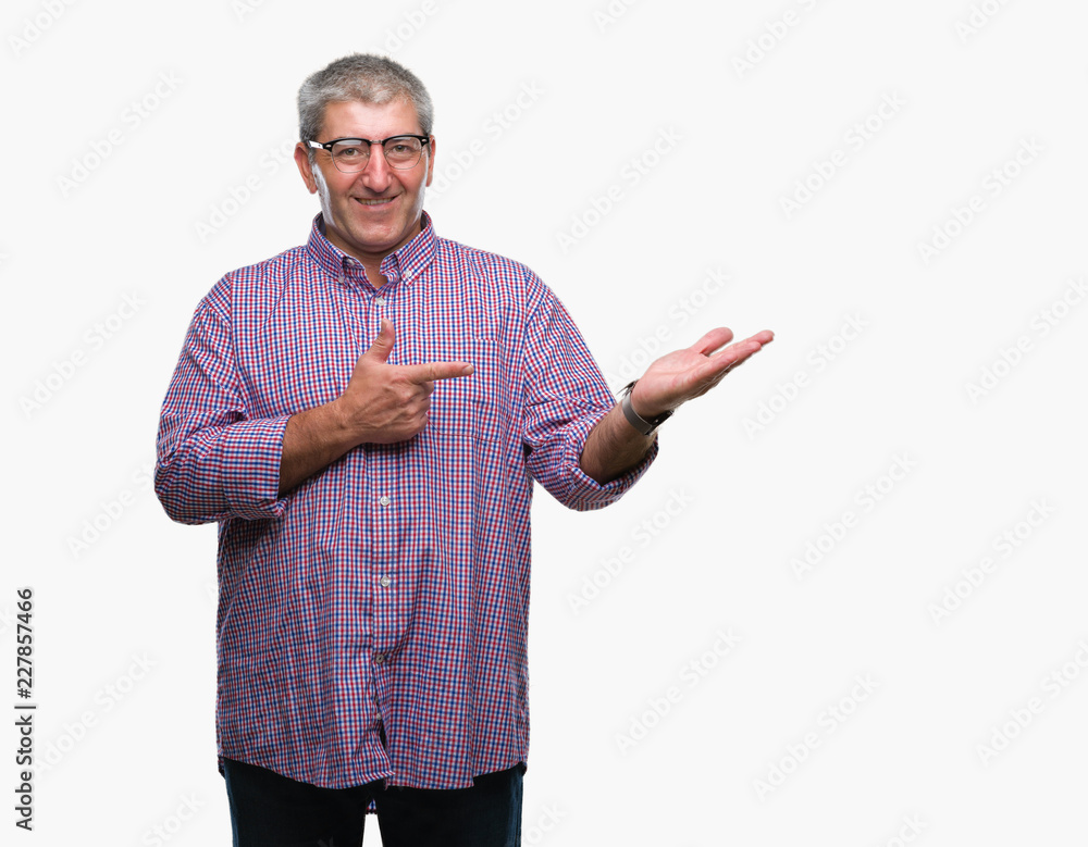 Handsome senior man wearing glasses over isolated background amazed and smiling to the camera while presenting with hand and pointing with finger.