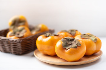 Ripe persimmon fruit on wooden plate and basket, healthy fruit