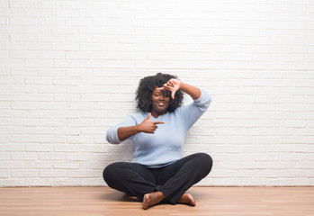 Sticker - Young african american woman sitting on the floor at home smiling making frame with hands and fingers with happy face. Creativity and photography concept.