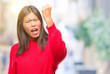 © Krakenimages.com - Young asian woman wearing winter sweater over isolated background angry and mad raising fist frustrated and furious while shouting with anger. Rage and aggressive concept.