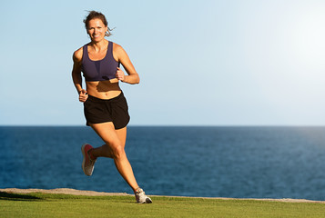 Fitness woman running by the ocean at sunset