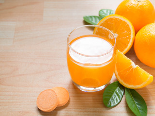 Vitamin c effervescent tablet is dissolving in glass of water w/ bubbles and fresh juicy orange fruits on wood table. Vitamin/mineral supplement, nutrition, health care and medical. Copy space.