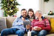 © Halfpoint - Small girl and her father and grandfather sitting on a sofa at Christmas, using tablet.