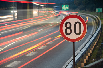 Long exposure shot of traffic sign showing 80 km/h speed limit on a highway full of cars in motion blur during the night