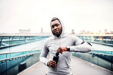 Wall Mural - A young sporty black man runner with water bottle in a city.