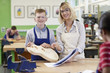 © highwaystarz - Portrait Of Female Teacher Helping Male High School Student Building Guitar In Woodwork Lesson