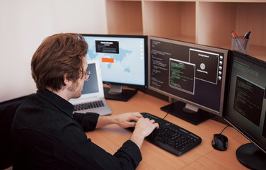 male programmer working on desktop computer with many monitors at office in software develop company