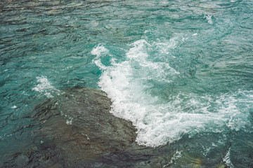 Detailed texture of turquoise rushing water surface. Rapids of mountain river close up. Background of clean water waves. Big boulder in creek with copy space.