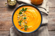 Delicious pumpkin cream soup in bowl on wooden background, top view