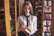 Young attractive student librarian reading a book between library bookshelves