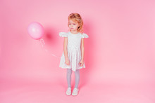 Sad Little Blonde Girl In White Dress In Peas 4-5 Year Old Holding Balloon In The Studio On A Pink Background,birthday Celebration ,sadness And Disappointment Sorrow