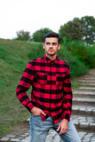 Fototapeta Młodzieżowe - Portrait of stylish male student with bread posing outdoors, looking at camera. Handsome man wearing in red checked shirt walking in autumn park. Concept of study, and mans fashion.