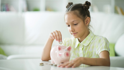 Wall Mural - Portrait of a cute little girl with a piggy bank