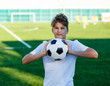 © Natali - cute young boy in white blue sportswear holds classical black and white football ball on the stadium field. Soccer game, training, hobby concept.