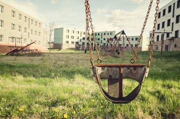 old swings in a park amongst long abandoned apartment buildings